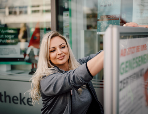 Person befestigt Informationsplakat an der Eingangstür der Althoff Apotheke in Neuwied.