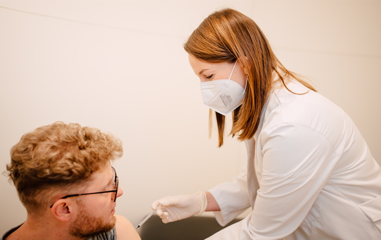 Impfung in der Althoff Apotheke Neuwied, medizinische Fachkraft verabreicht Spritze an Kunden im Behandlungsraum.
