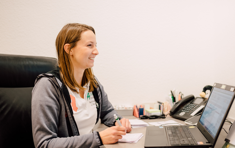 Mitarbeiterin der Althoff Apotheke arbeitet am Schreibtisch mit Laptop und Unterlagen im Bürobereich.